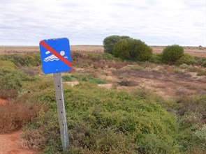 Warning sign at the earthen tank near the yellow bus